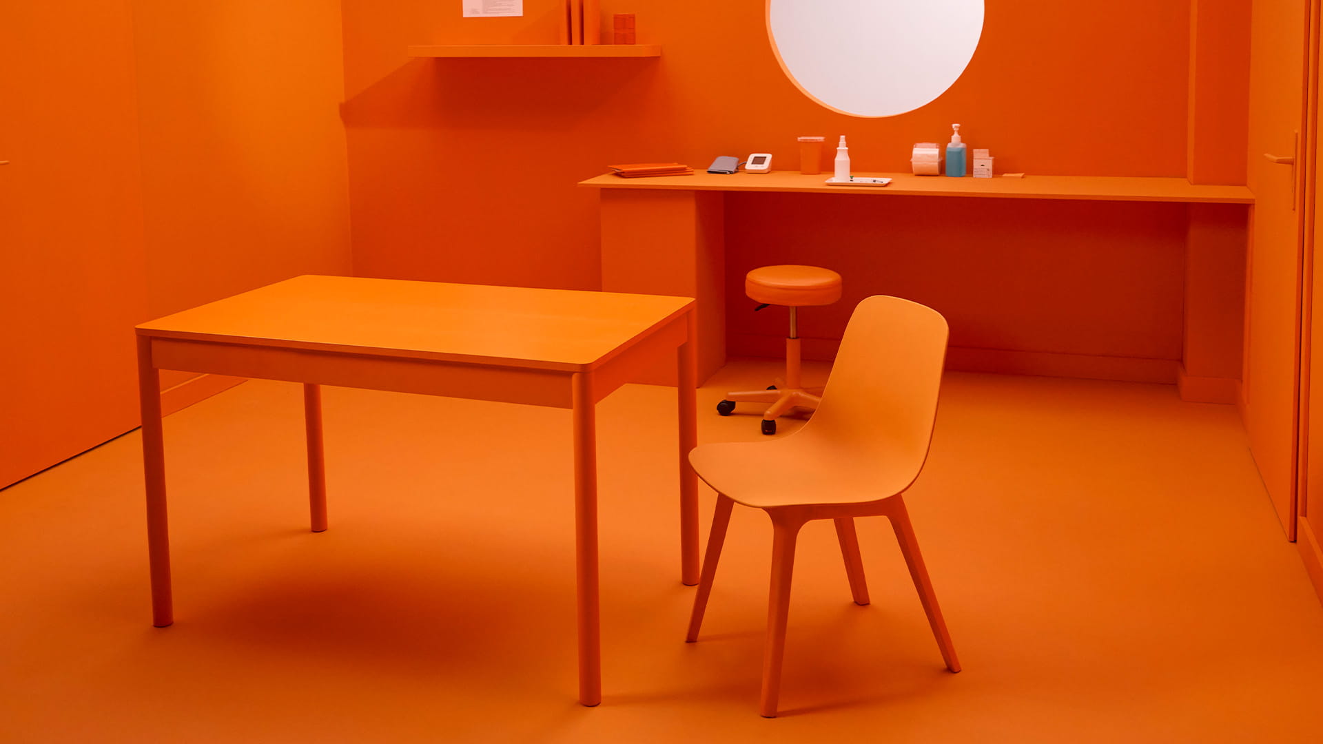 Stilisiertes Impfzimmer in Orange mit Tisch und Stuhl im Vordergrund. 